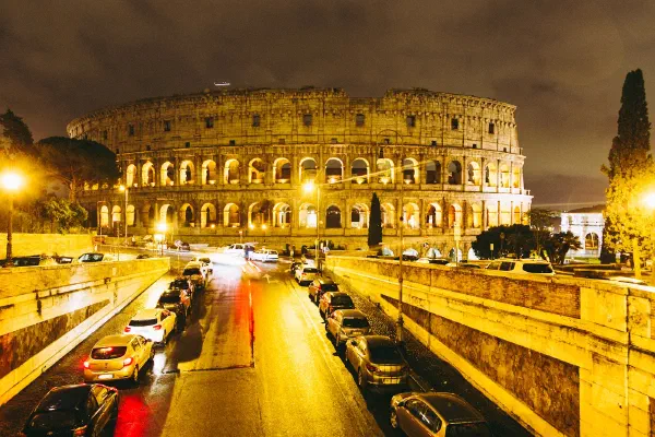 The Colosseum illuminated at night, with traffic on the road below.