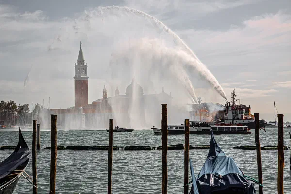 Boats spray arcs of water across a waterfront, with a bell tower in the distance.
