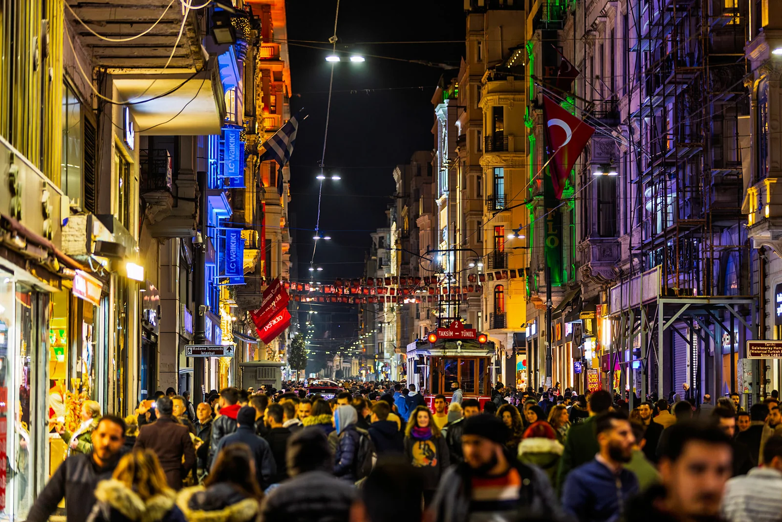 A crowded narrow street glowing with coloured lights at night.