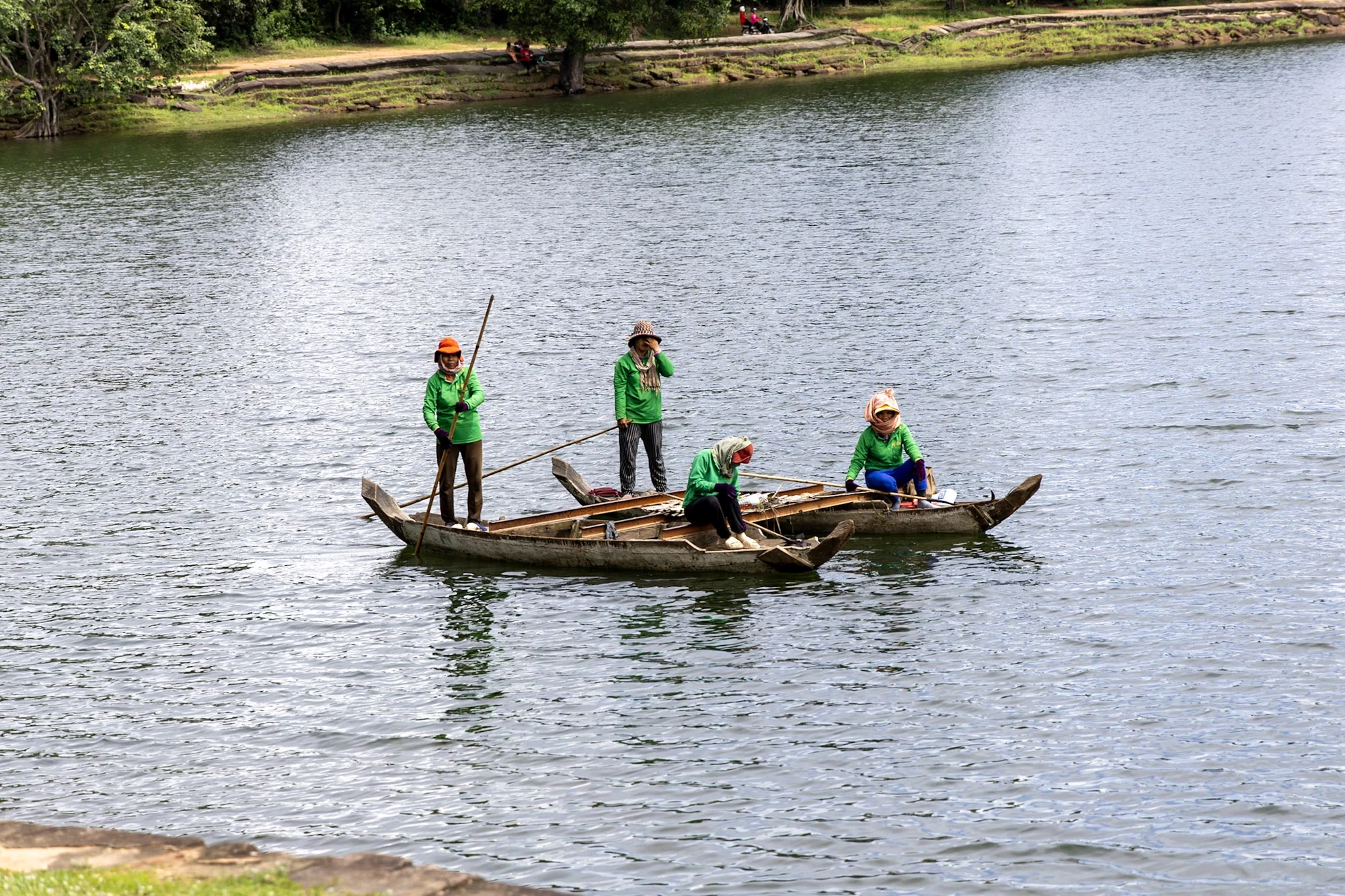 Workers in green shirts crossing the water in a wooden boat.