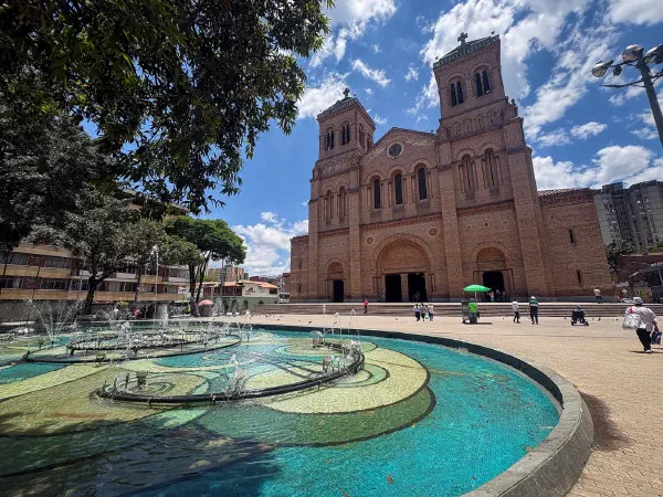 A brick church beyond a fountain in a tree-lined square.