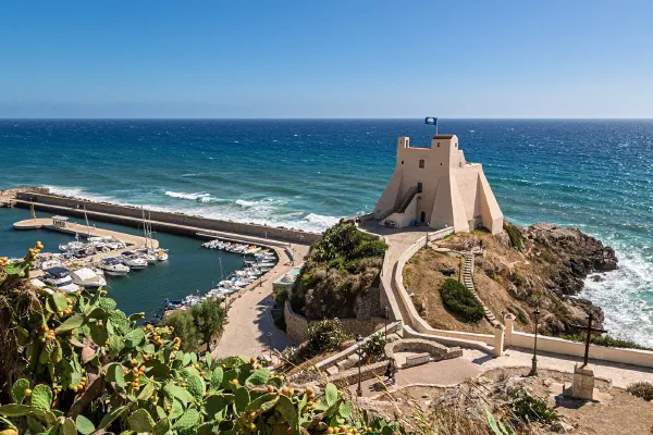 A coastal watchtower above a harbour and turquoise sea.