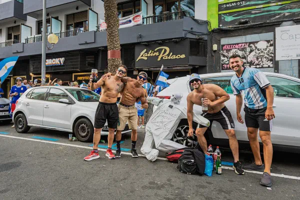 A group of people celebrating beside a parked car.