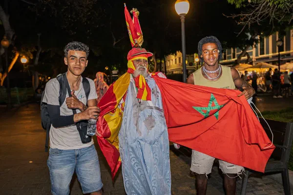Three people displaying Spanish and Moroccan flags at night.