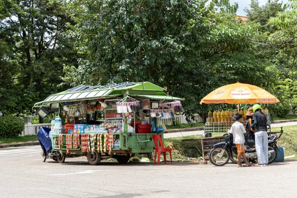 Customers beside a roadside drinks cart and a yellow umbrella.
