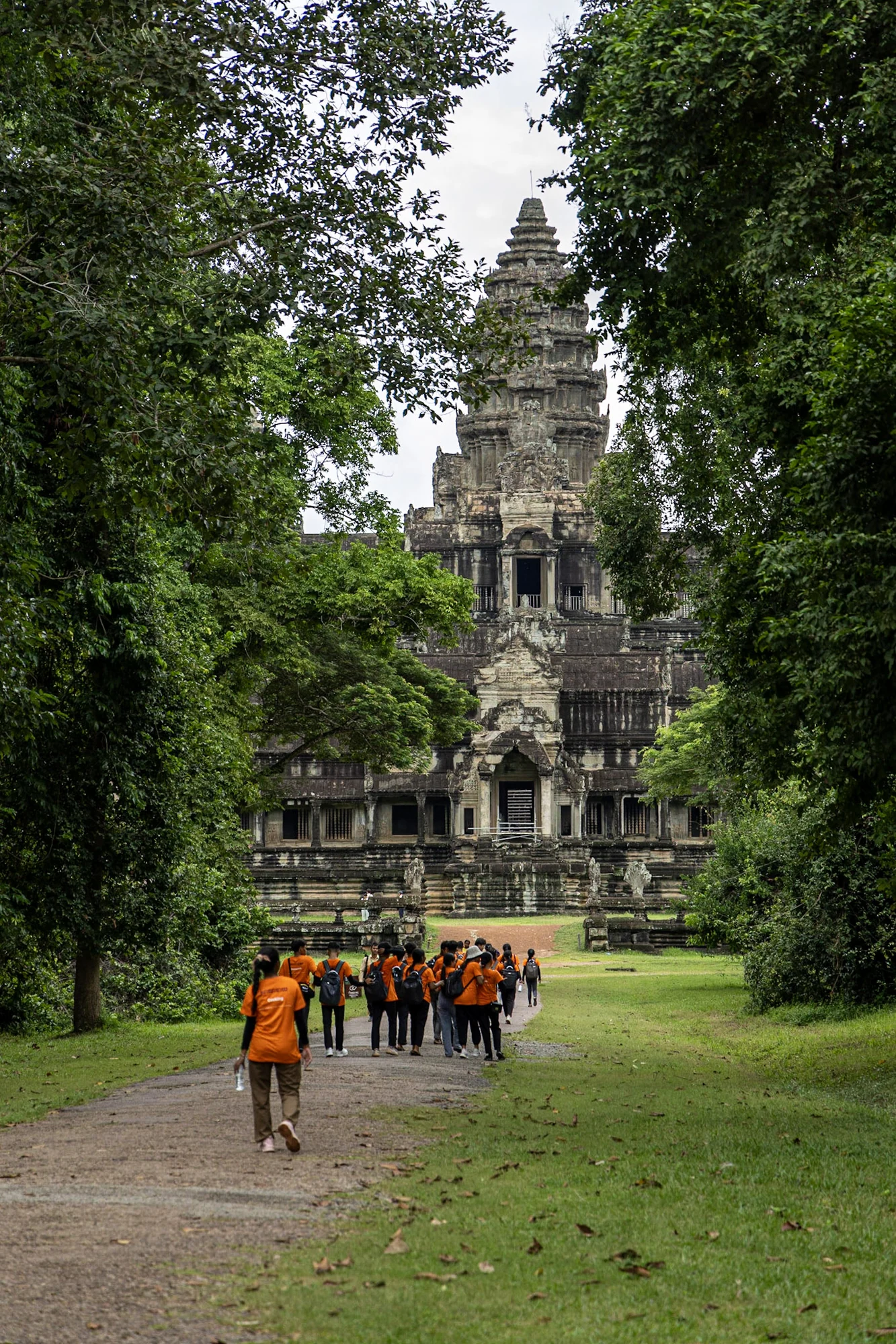 A group in orange robes walking towards a temple tower between trees.