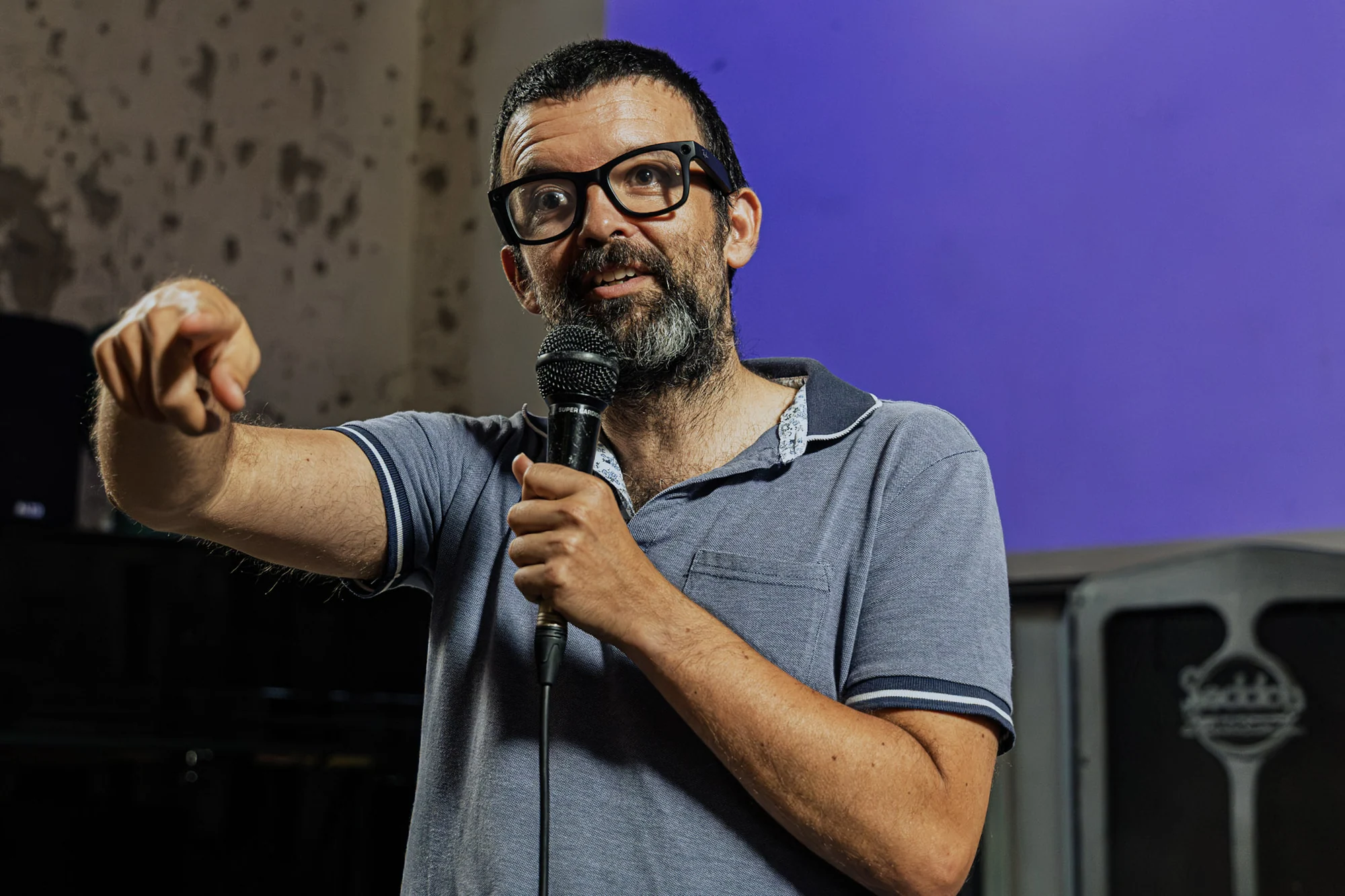 A speaker holding a microphone and pointing towards the audience.