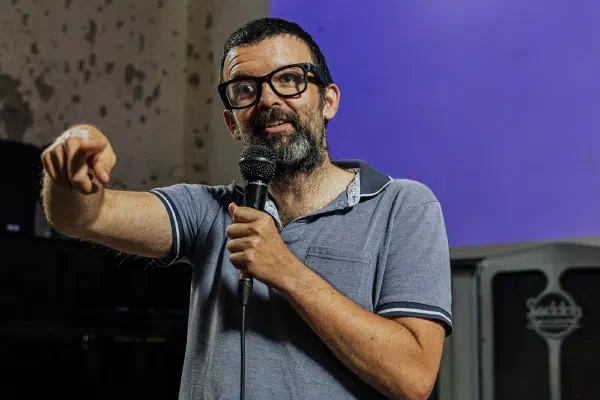 A speaker holding a microphone and pointing towards the audience.