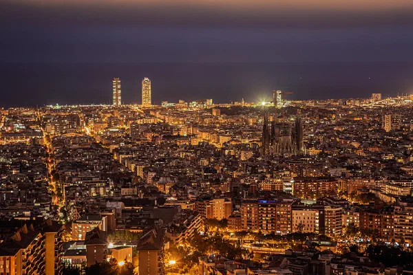 A dense city seen from above at dusk, with twin towers on the horizon.