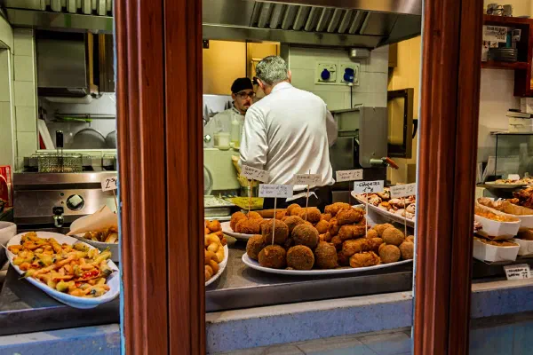 A cook working behind a counter filled with fried food.
