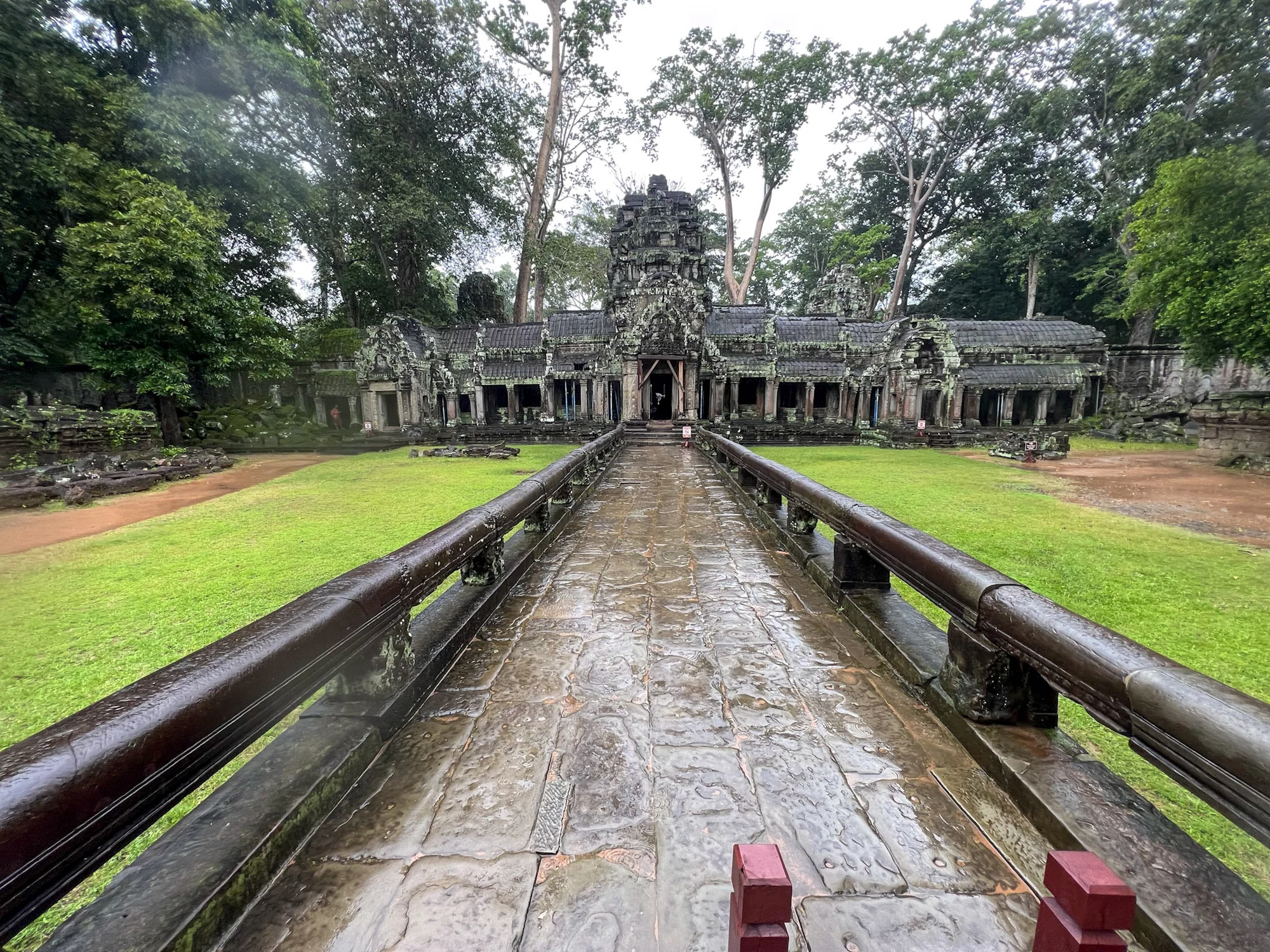 A wet stone causeway leading towards a temple surrounded by trees.