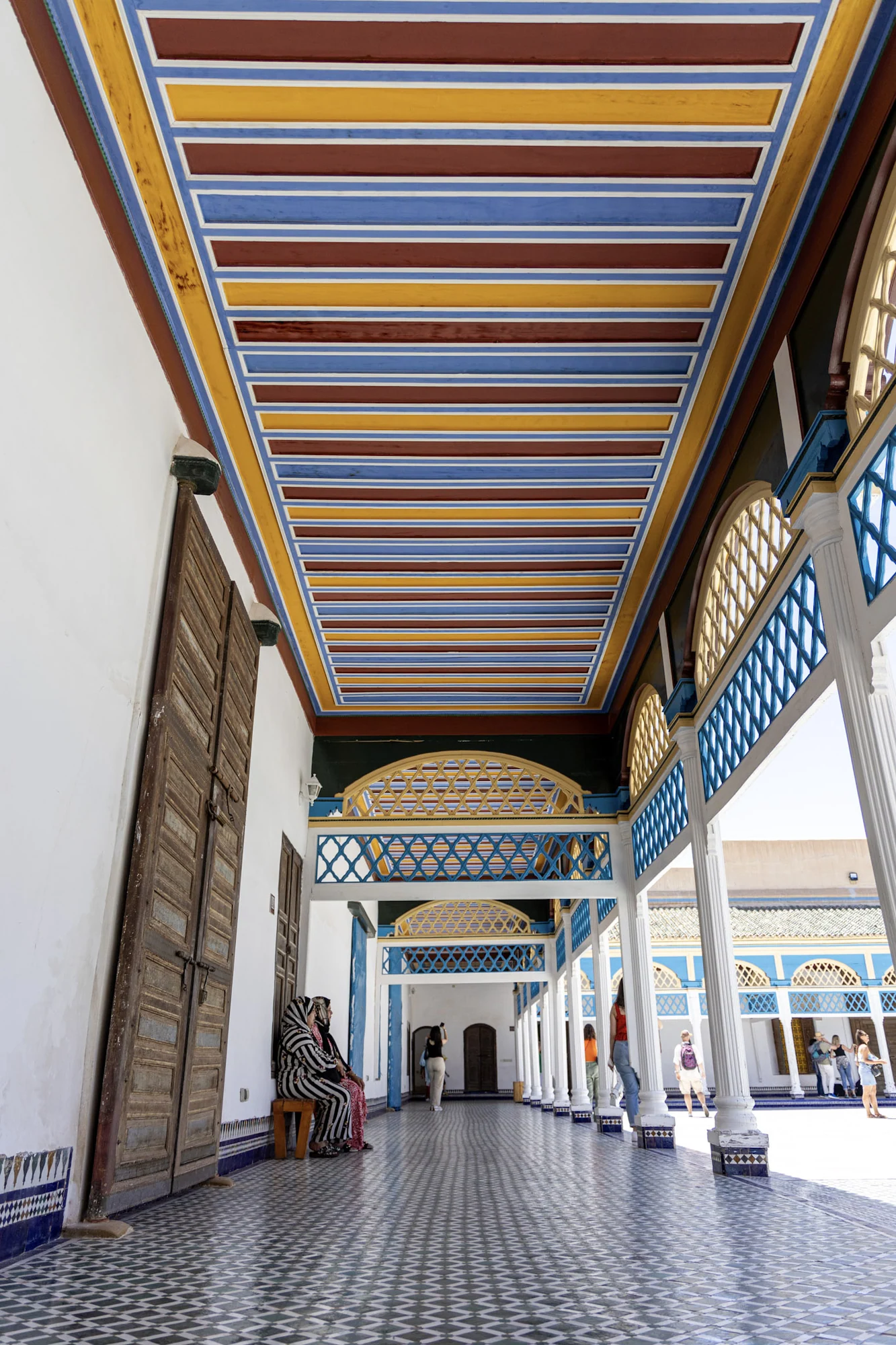 A palace colonnade with a colourful painted ceiling and patterned tiles.