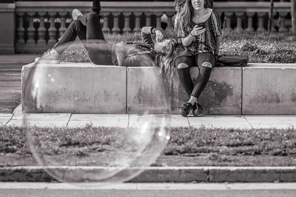 A large soap bubble floating in front of people on stone steps.