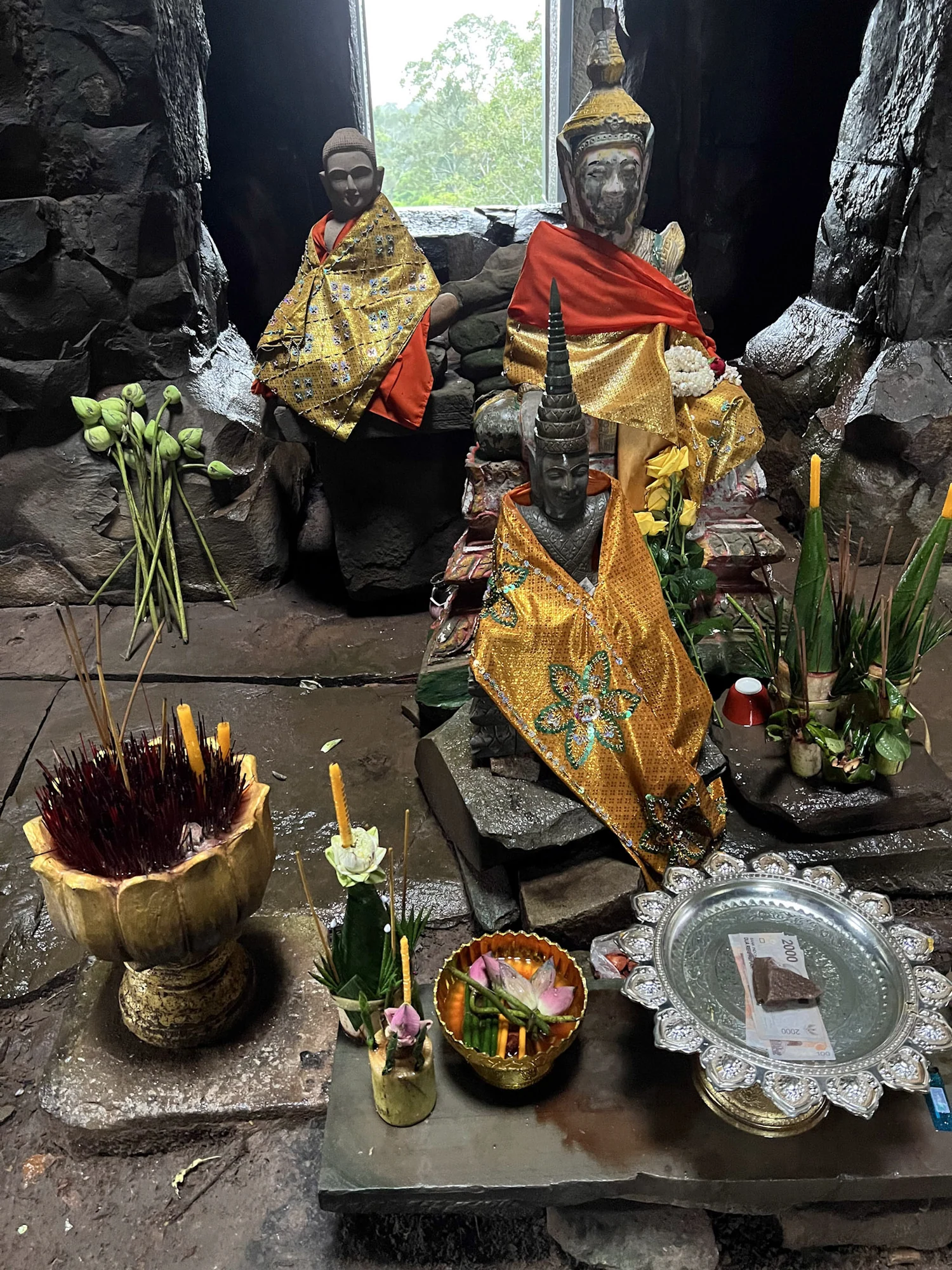 Cloth-draped statues and offerings inside a small temple shrine.