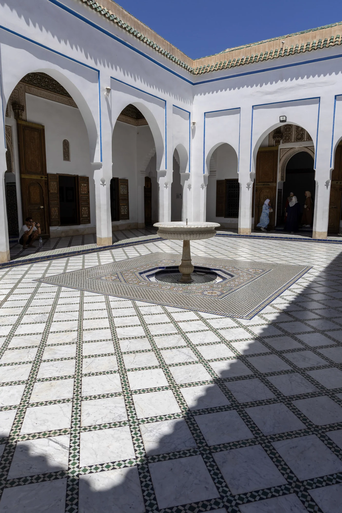 Sunlight and a lattice shadow cross a tiled courtyard with white arches.