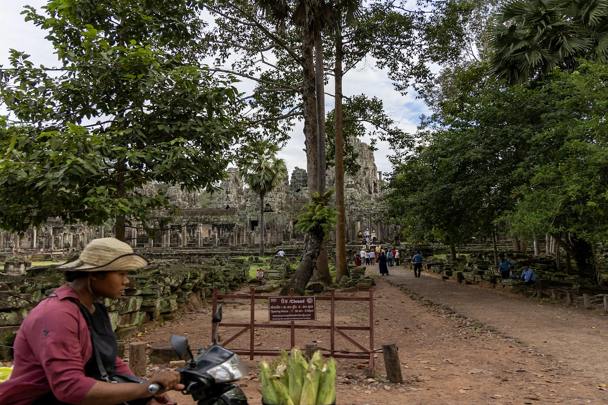 A vendor with a motorbike beside a tree-lined temple approach.