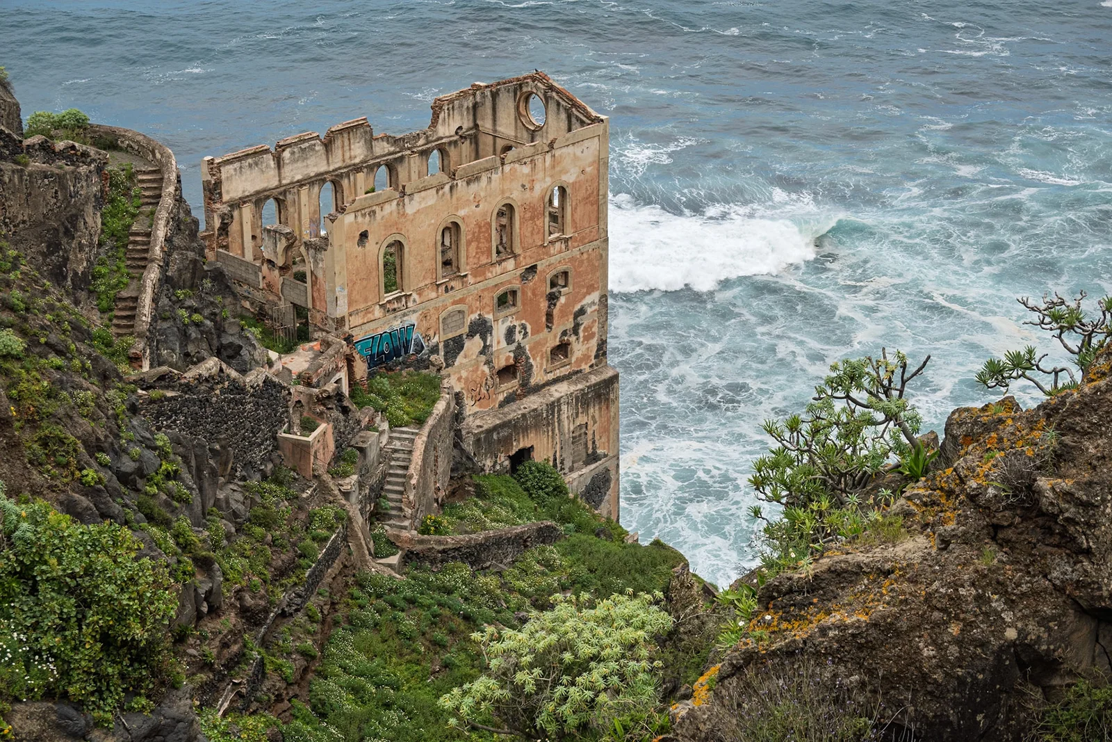 An old building clinging to a coastal cliff above the sea.