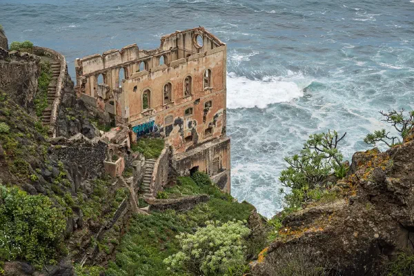 An old building clinging to a coastal cliff above the sea.